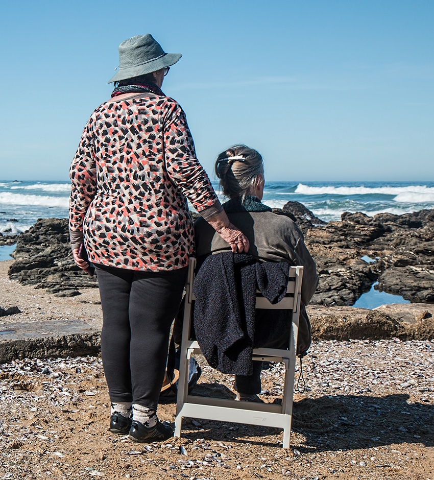 an elderly with a caregiver beside at the sea