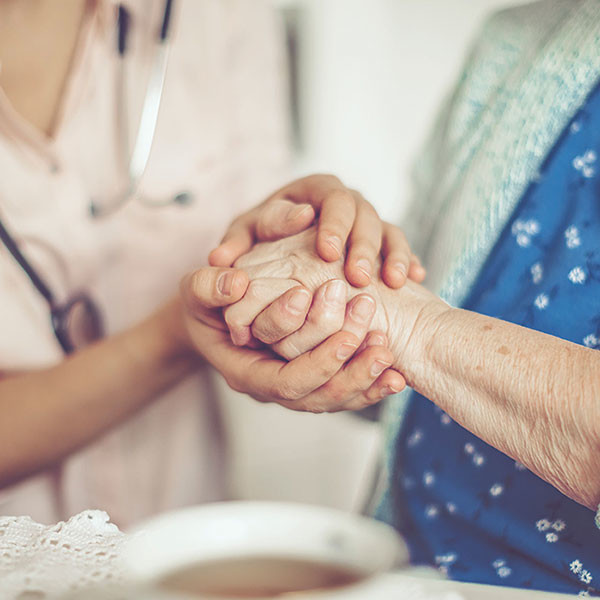 caregiver holding the hand of an elderly woman