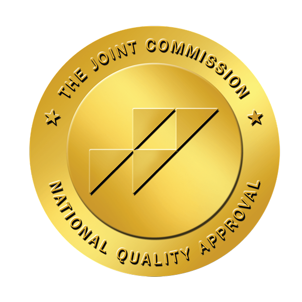 A gold circular seal with the text The Joint Commission National Quality Approval surrounding an abstract geometric logo in the center, symbolizing excellence in home care.